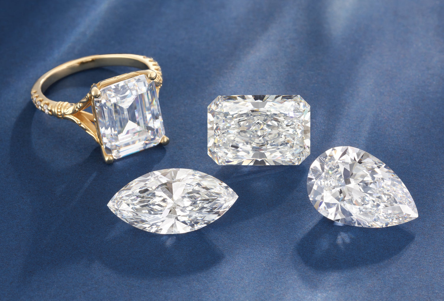 Gold ring with diamond and three loose diamonds on a blue fabric background